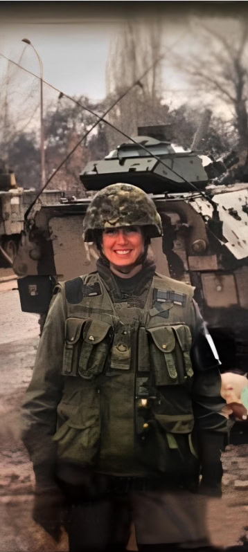 A woman veteran standing in front of military equipment in-field.