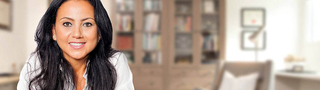 A professional woman with long dark hair, wearing a white blouse, smiling confidently in a warm and welcoming office setting after participating in services like EMDR therapy near me.