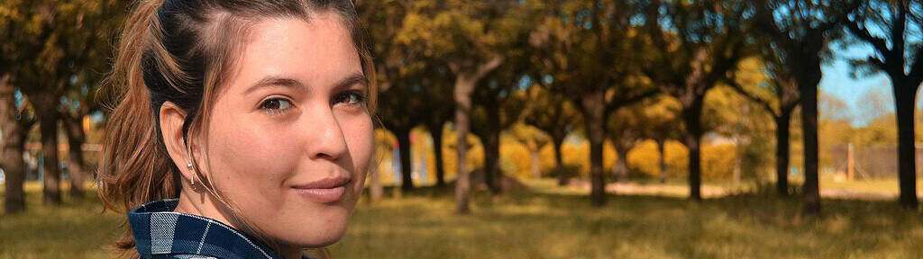 A thoughtful woman sitting outdoors in a sunlit park, symbolizing reflection and healing, representing the concept of how EMDR therapy differs from Trauma-Informed counselling.