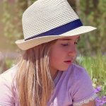 A young girl wearing a straw hat and a light purple shirt sits cross-legged on a small suitcase in a garden with colourful flowers. She appears to be deep in thought, symbolising the calm and introspective nature of EMDR therapy for children.