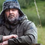 A man wearing a winter hat and jacket leaning on a wooden fence in a rural setting, symbolizing contemplation and decision-making, possibly reflecting on in-person vs online EMDR therapy options.