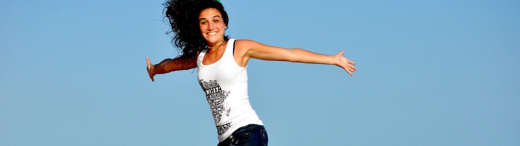 A joyful woman jumping on a beach with arms outstretched, symbolizing emotional freedom and well-being, aligning with the concept of understanding EMDR therapy.