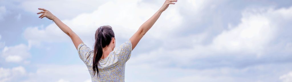 A woman standing in a field with her arms raised, symbolizing freedom and personal growth. The image represents recovery from codependency and addiction, highlighting empowerment, healing, and a fresh start toward emotional independence.