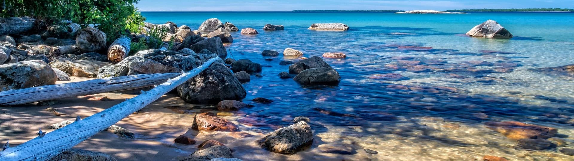 Serene shoreline scene with clear blue water and scattered rocks, representing the calming beach room atmosphere at AERCS Therapy Orangeville.