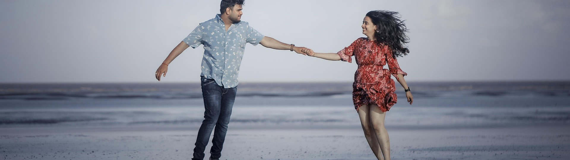 A smiling couple holding hands and running along the shoreline, illustrating the importance of shared experiences to strengthen your relationship.