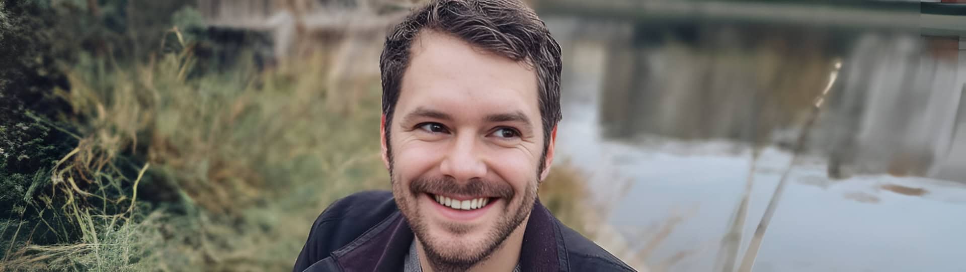 Smiling man outdoors near a small lake, representing hope and recovery with the best EMDR therapist in Orangeville.