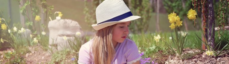 Young girl sitting quietly in a flower garden wearing a striped sunhat, representing the thoughtful comparison in the blog post titled EMDR Therapy for Children vs. Trauma-Informed Care: Which is Right for Childhood Trauma?