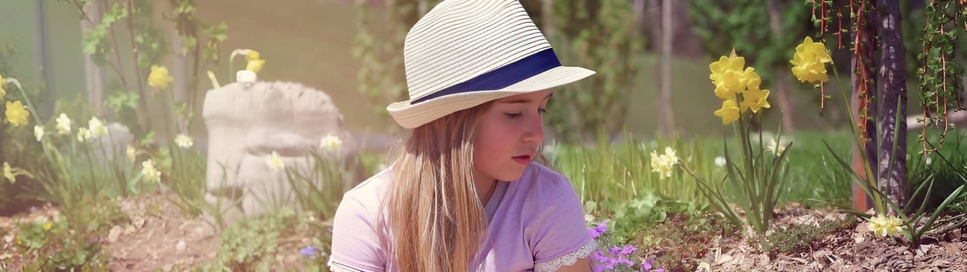 Young girl sitting quietly in a flower garden wearing a striped sunhat, representing the thoughtful comparison in the blog post titled EMDR Therapy for Children vs. Trauma-Informed Care: Which is Right for Childhood Trauma?
