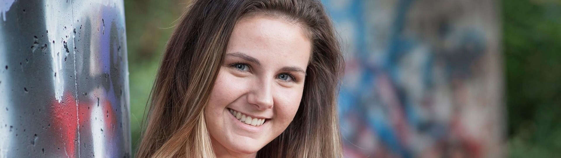 Smiling young woman outdoors in front of colourful graffiti, representing confidence and positive progress during anxiety therapy length.