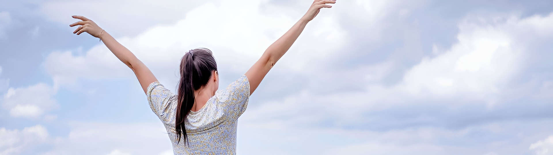 Woman standing with arms raised under a cloudy sky, representing emotional freedom and personal growth in the context of understanding codependency and addiction.