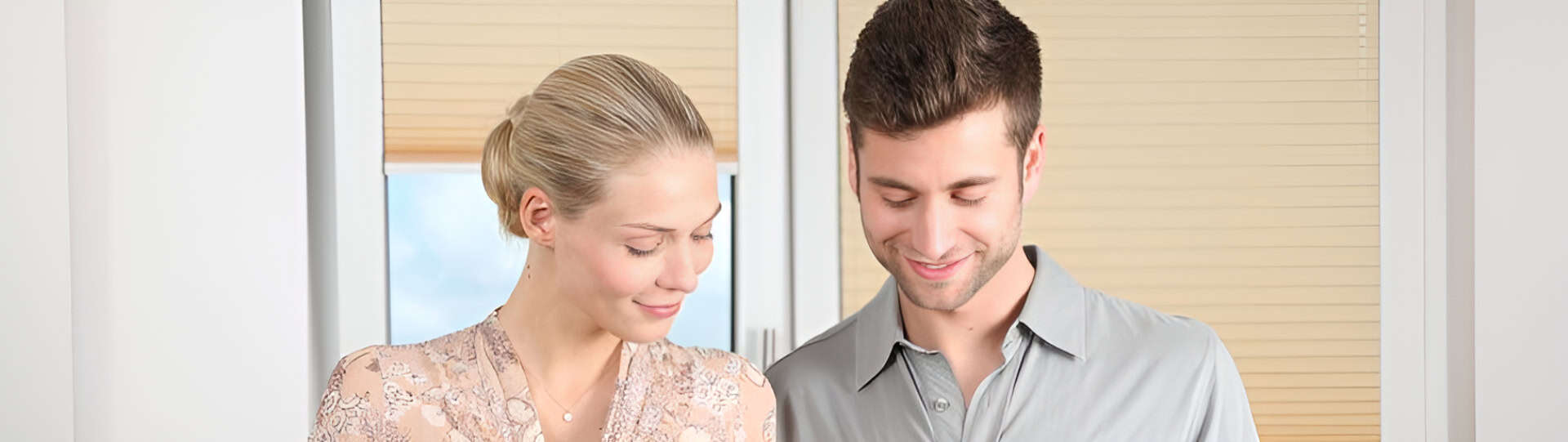 A couple standing together indoors, smiling and looking down, representing healthy communication in marriage through mutual understanding and emotional connection.