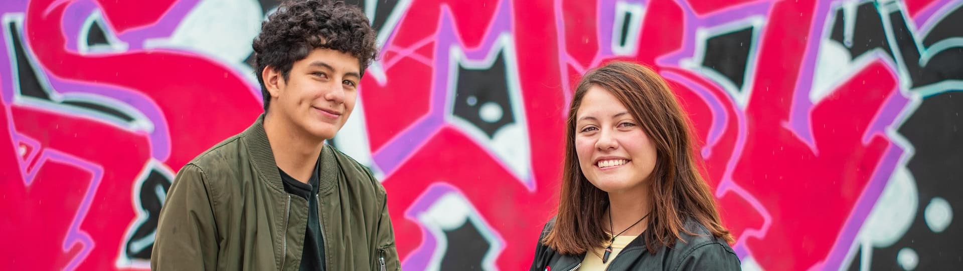 Smiling young couple standing in front of a colourful graffiti wall, suggesting openness to answering couples therapy questions together.