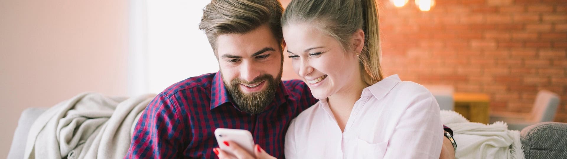 Smiling couple sitting on a couch looking at a phone together, representing a positive outcome after attending their first couples counselling session.