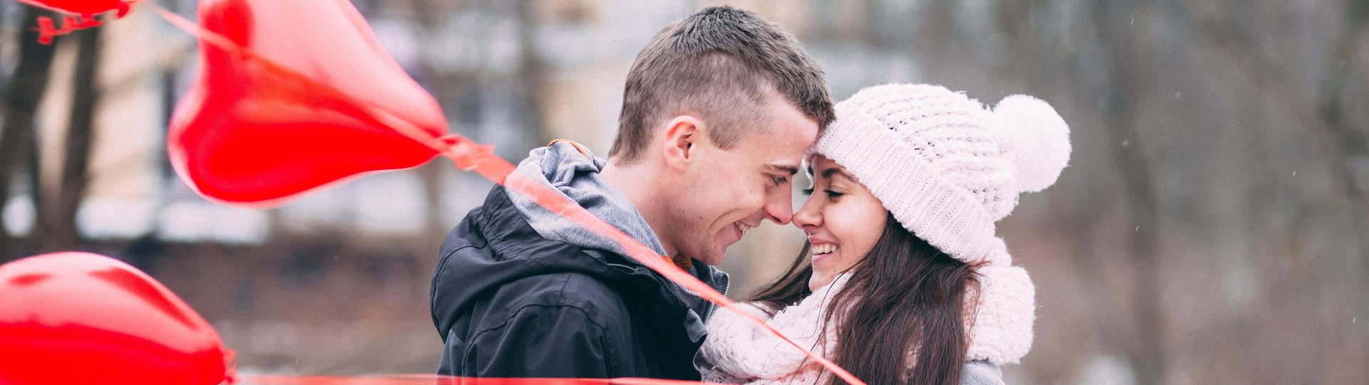 A happy couple embracing outdoors in winter with red heart balloons, symbolizing emotional reconnection and healing through couples counselling.