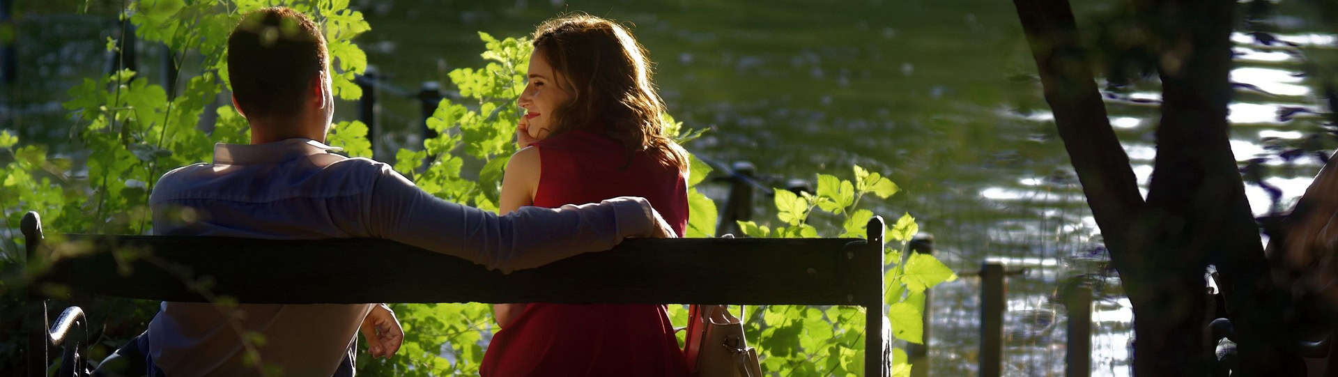 A couple sitting on a bench talking calmly beside a peaceful lake, symbolising open communication and therapist neutrality in relationship counselling.